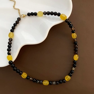 Handmade beaded necklace with yellow resin pendant and black agate beads on white plate