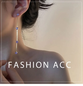 Detalle de pendientes largos dorados con cuatro circonitas púrpuras en una modelo