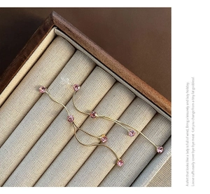 Detalle de pendientes dorados con borlas y cuatro cristales rosas sobre base lino