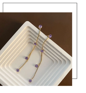 Primer plano de pendientes largos de borla dorada con circonitas púrpuras en cadena