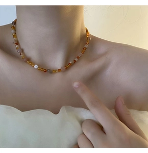 Dettaglio della collana di perline ambra e marroni sulla clavicola di una modella