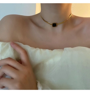 Gros plan d'un collier chaîne serpent dorée avec pendentif carré noir sur un mannequin