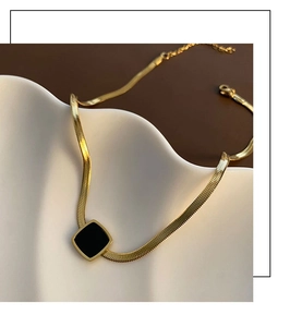 Détail d'un collier chaîne serpent dorée avec pendentif carré noir sur plateau céramique