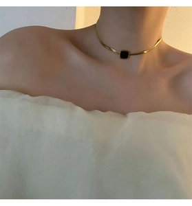 Gros plan d'un collier chaîne serpent dorée avec un pendentif carré en onyx noir