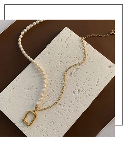 Detail of asymmetric pearl necklace with gold chain and rectangular textured pendant