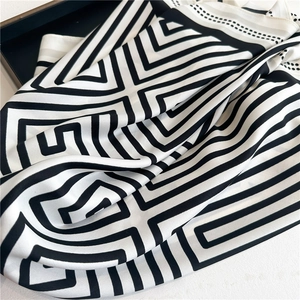 Detail eines schwarz-weißen Seidenschals mit geometrischen Streifen und Satin-Textur