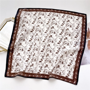 Détail d'un foulard carré avec motifs vintage marron sur fond blanc et texture soyeuse