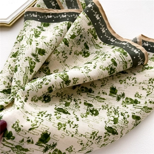 Détail de la texture du foulard ivoire avec motif paysage vert et bordures dorées