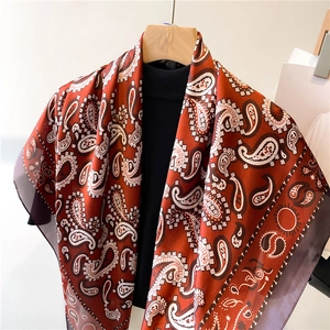 Classic paisley print silk-like scarf in vintage orange, draped on a wooden hanger