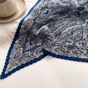 Détail d'un foulard en soie plissé avec motif bleu sur une surface en peluche blanche