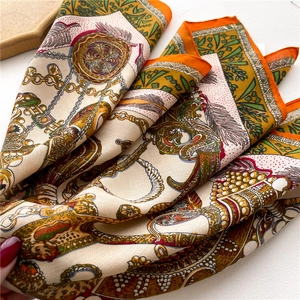 Close-up of silk-textured scarf showing classic harness print and luxury golden chain details
