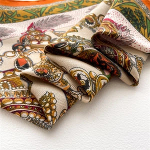 Detailed view of luxury twill silk scarf featuring royal emblems and orange borders