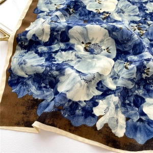 Detail of floral silk scarf showing white flowers and birds on a blue fabric background