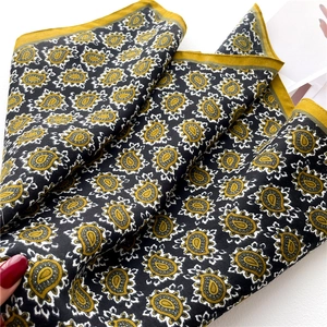 Close-up of a black paisley silk scarf with mustard yellow borders and twill texture