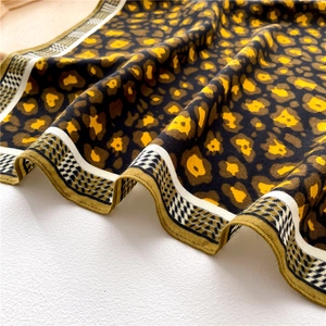 Macro detail of silk scarf showing yellow leopard print and geometric patterned border