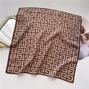 Detailed view of brown and beige square silk scarf with geometric pattern on a magazine