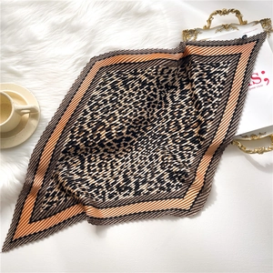 Elegant leopard print pleated square scarf with orange borders on a white plush background