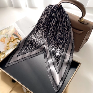 Leopard print pleated silk scarf tied on a brown leather handbag in luxury setting
