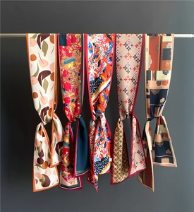 Détail de cinq foulards étroits aux motifs variés suspendus sur une barre métallique argentée