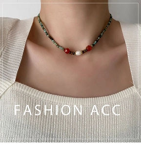 Détail d'un collier de perles vertes avec une perle blanche et des pierres rouges