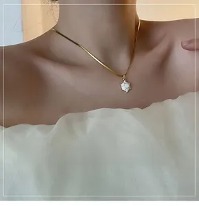 Detail view of a white turtle pendant on a golden snake chain necklace worn by a model