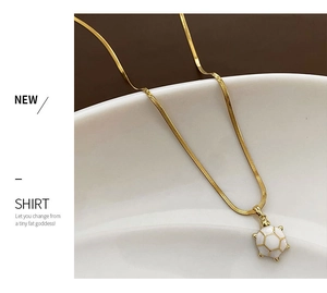 Close-up of golden snake chain necklace with a white enamel turtle pendant on a ceramic dish