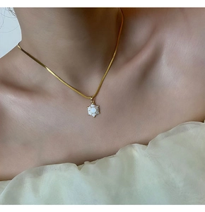 Close-up of a delicate gold snake chain necklace with a white turtle shell pendant on neck