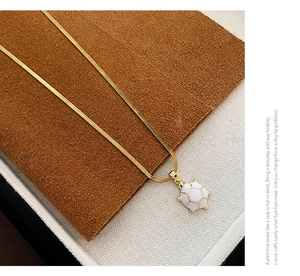 Close-up of golden turtle pendant with white enamel shell on a dainty snake chain