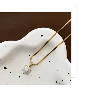 Macro detail of a golden turtle pendant with white enamel inlay on a thin snake chain