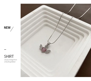 Macro detail of silver necklace with pink heart gem and diamond-set wings on a white stand