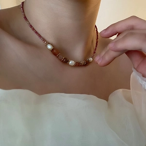 Collier élégant avec perles rouges, blanches et pierres brunes sur le cou d'un modèle