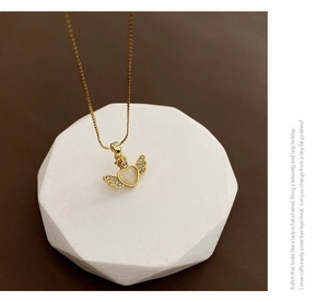 Close-up of golden necklace with winged heart crown pendant and opal gemstone on marble