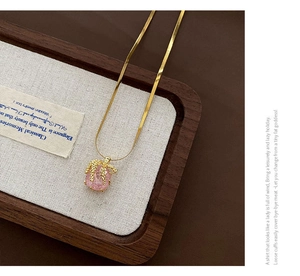 Gros plan du pendentif en zircon rose sur chaîne dorée dans un plateau en bois de noyer