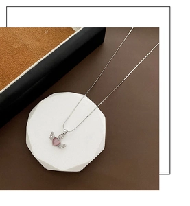 Detail of silver angel wing necklace featuring a pink heart pendant on stone display