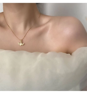 Detailed view of a gold heart necklace with wing accents and gems on a model neck