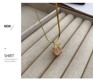 Gros plan du pendentif cristal rose avec feuilles dorées sur une chaîne serpent dorée