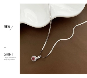Macro detail of red heart zircon pendant on a silver herringbone flat snake chain