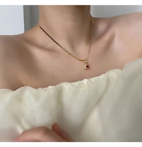 Detail of a red zircon pendant on a gold snake chain necklace worn by a female model