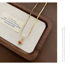 Detail of a gold snake chain necklace with a luxury red gemstone and white diamond halo