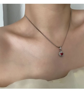 Close-up of heart-shaped red zircon pendant on a silver-tone chain worn by model