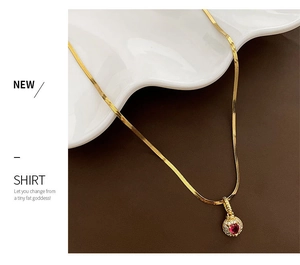 Detail of gold snake chain necklace featuring a red heart zircon pendant with halo stones