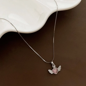 Elegant angel wing heart necklace with pink gemstone and crown detail on white ceramic