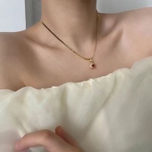 Elegant gold snake chain necklace with a round red zircon pendant worn by a model