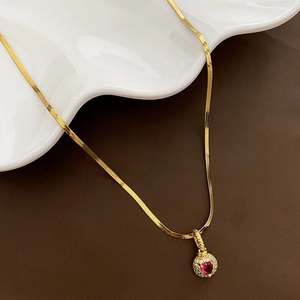 Gold necklace with red heart zircon pendant on white wavy tray, 45-degree angle
