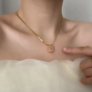 Pendentif en zircon rose sur chaîne serpent dorée porté avec une tenue blanche