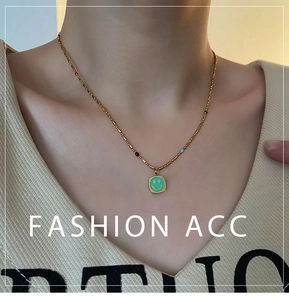 Dettaglio della collana dorata con perle colorate e ciondolo quadrato verde con smile