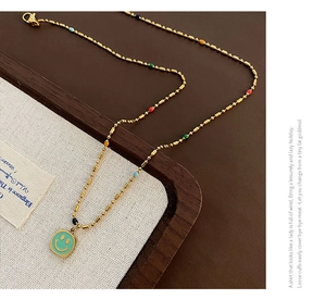 Dettaglio della collana dorata con perle multicolori e ciondolo smiley in smalto verde