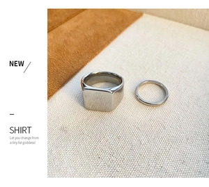 Close-up of polished gold square signet ring and thin band on textured fabric