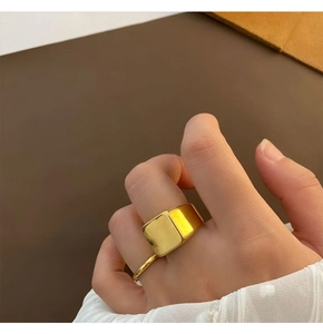 Close-up of a wide square-faced gold titanium signet ring worn on the index finger