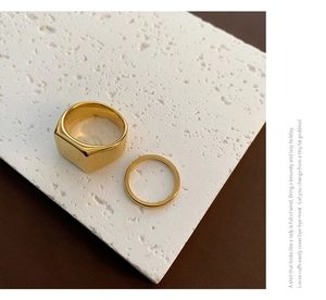 Detail of heavy gold geometric signet ring and slim round band on textured stone